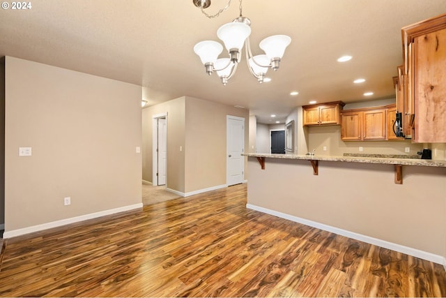 kitchen with a breakfast bar, kitchen peninsula, light stone countertops, wood-type flooring, and a chandelier