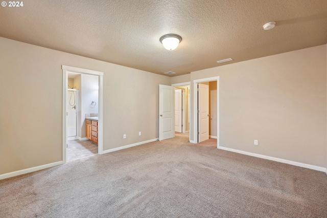 unfurnished bedroom with a textured ceiling, light carpet, and ensuite bath