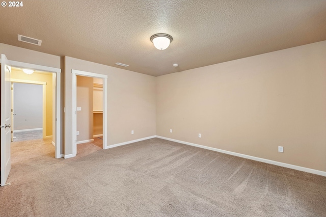 unfurnished bedroom with a textured ceiling, a walk in closet, light colored carpet, and a closet