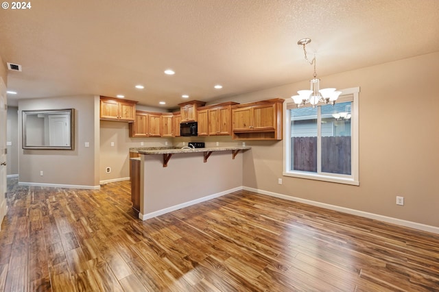 kitchen with dark wood-type flooring, hanging light fixtures, a notable chandelier, kitchen peninsula, and a breakfast bar area