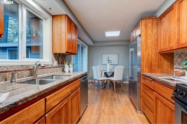 kitchen featuring stainless steel appliances, sink, light stone counters, tasteful backsplash, and light hardwood / wood-style flooring