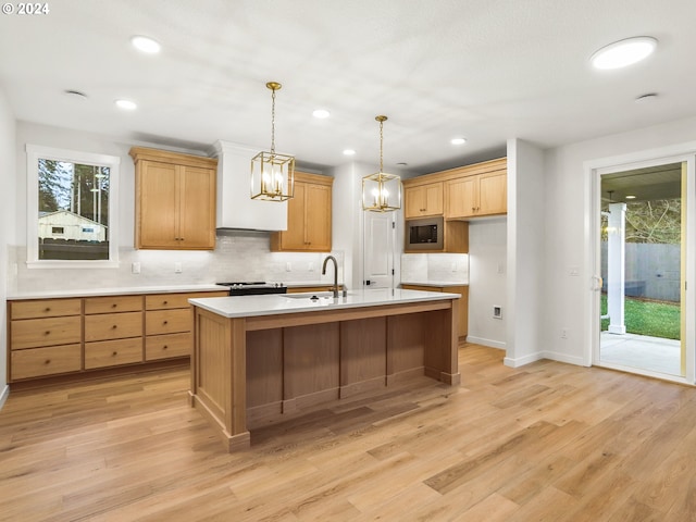 kitchen featuring sink, stainless steel microwave, light hardwood / wood-style flooring, an island with sink, and pendant lighting