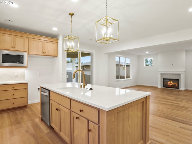 kitchen with a tile fireplace, built in microwave, sink, an inviting chandelier, and an island with sink