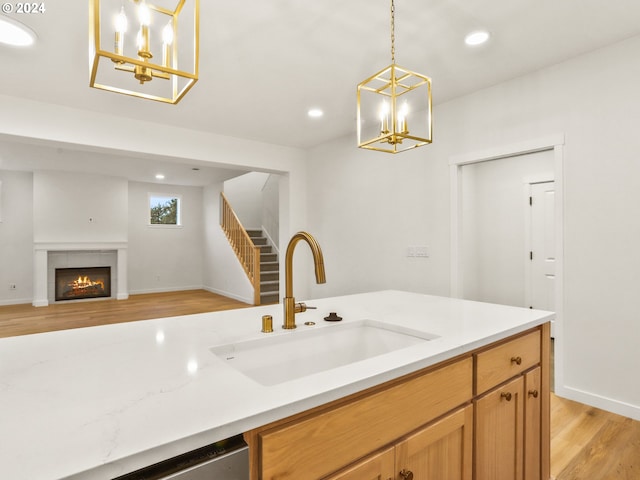 kitchen with a tile fireplace, sink, hanging light fixtures, stainless steel dishwasher, and light wood-type flooring