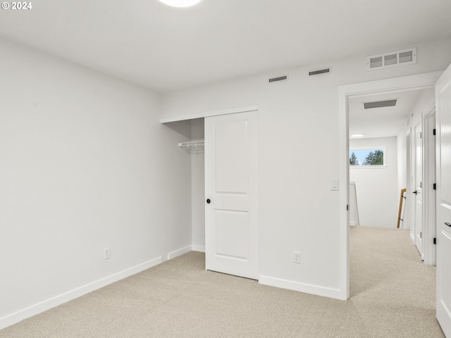 unfurnished bedroom with light colored carpet and a closet