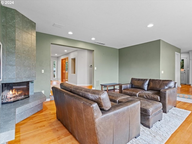 living room featuring a tiled fireplace, light hardwood / wood-style flooring, and plenty of natural light