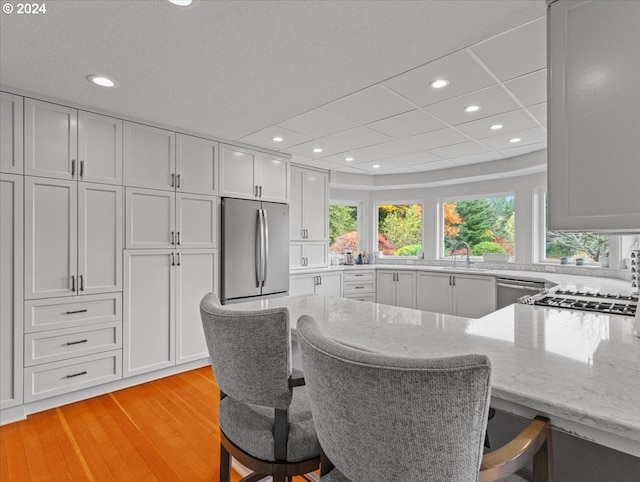 kitchen featuring light stone counters, white cabinets, a breakfast bar, light hardwood / wood-style flooring, and stainless steel fridge