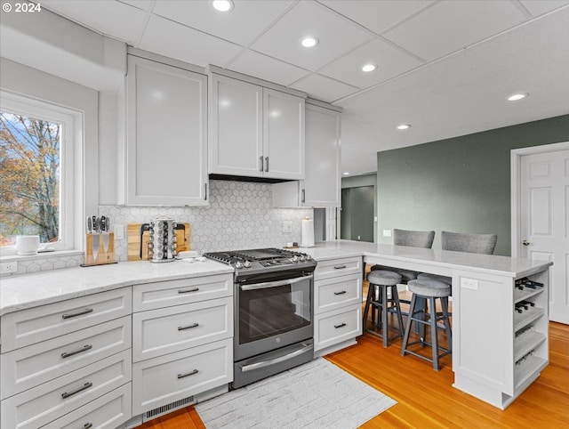 kitchen with a kitchen bar, light hardwood / wood-style floors, white cabinets, gas stove, and backsplash