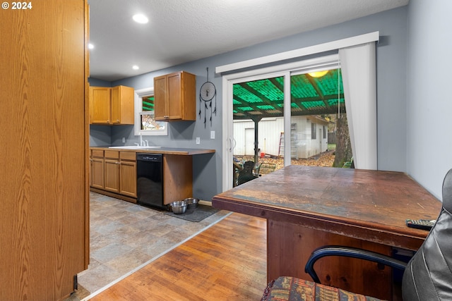 kitchen featuring a textured ceiling, sink, black dishwasher, and light hardwood / wood-style flooring