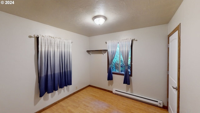 spare room with a textured ceiling, hardwood / wood-style flooring, and a baseboard heating unit