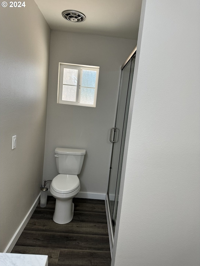 bathroom with wood-type flooring, toilet, and a shower with door