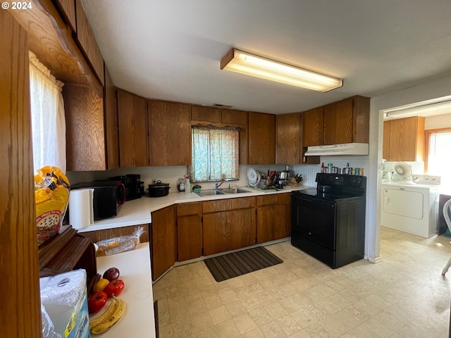 kitchen featuring washer and clothes dryer, light floors, black / electric stove, under cabinet range hood, and a sink