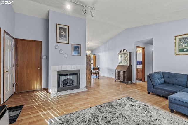 living room featuring a textured ceiling, vaulted ceiling, hardwood / wood-style flooring, a chandelier, and a tiled fireplace