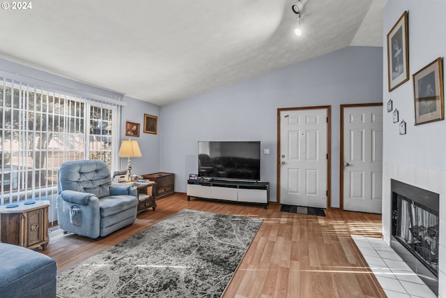 living room with a tile fireplace, a textured ceiling, light hardwood / wood-style floors, and vaulted ceiling