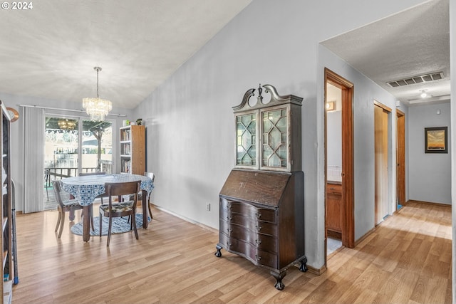 dining room with a textured ceiling, light wood-type flooring, and an inviting chandelier