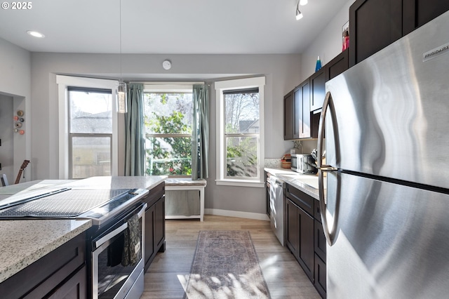 kitchen with dark brown cabinetry, appliances with stainless steel finishes, decorative light fixtures, and light hardwood / wood-style floors