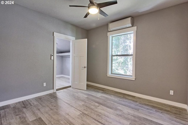 unfurnished bedroom featuring ceiling fan, light wood-type flooring, a closet, and an AC wall unit