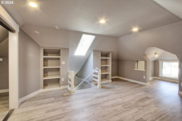 bonus room featuring built in shelves, lofted ceiling with skylight, and light hardwood / wood-style floors