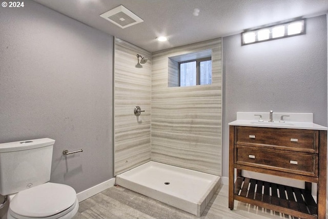 bathroom with hardwood / wood-style flooring, vanity, toilet, and a tile shower