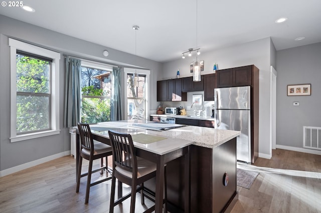 kitchen with a kitchen island, decorative light fixtures, a breakfast bar area, stainless steel fridge, and dark brown cabinets