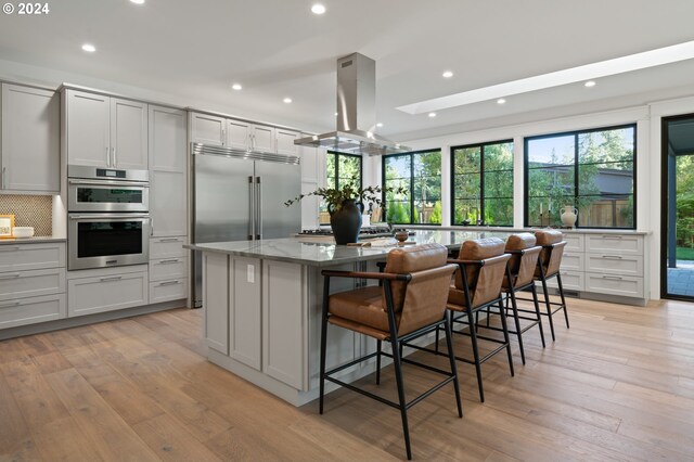 kitchen with appliances with stainless steel finishes, a kitchen island, island exhaust hood, and light hardwood / wood-style flooring