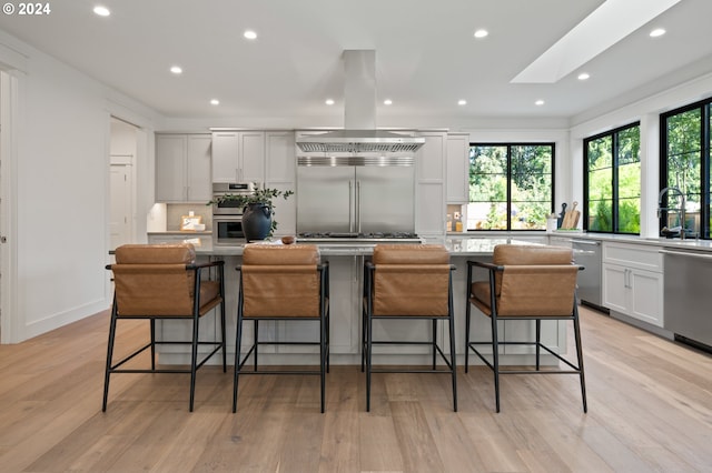 kitchen with island exhaust hood, appliances with stainless steel finishes, white cabinets, a kitchen island, and a kitchen bar