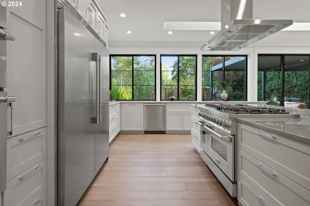 kitchen with white cabinets, high end appliances, light wood-type flooring, light stone counters, and island exhaust hood