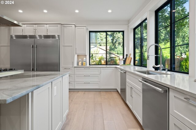 kitchen featuring light hardwood / wood-style flooring, appliances with stainless steel finishes, light stone counters, sink, and exhaust hood