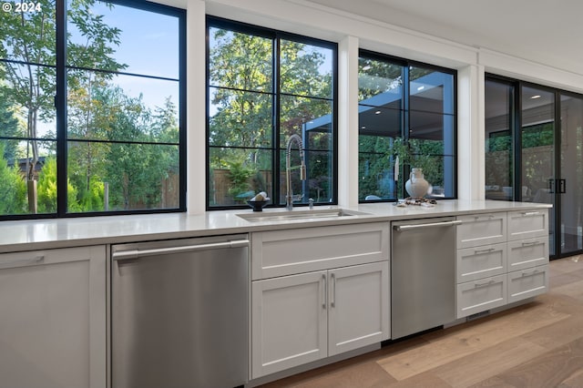 kitchen featuring light wood finished floors, light countertops, white cabinetry, a sink, and dishwasher