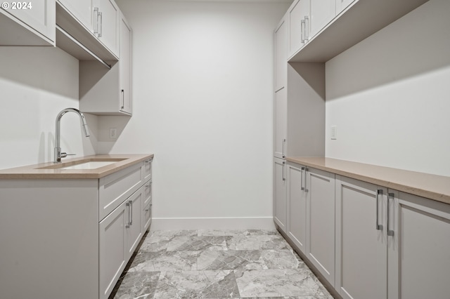 kitchen featuring baseboards, white cabinetry, light countertops, and a sink