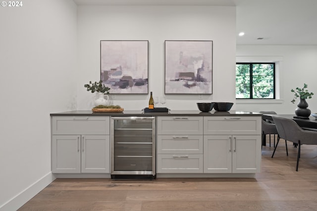 bar with beverage cooler, baseboards, a bar, light wood-style floors, and recessed lighting