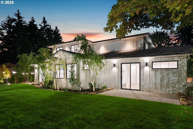 back house at dusk featuring a lawn and a patio area