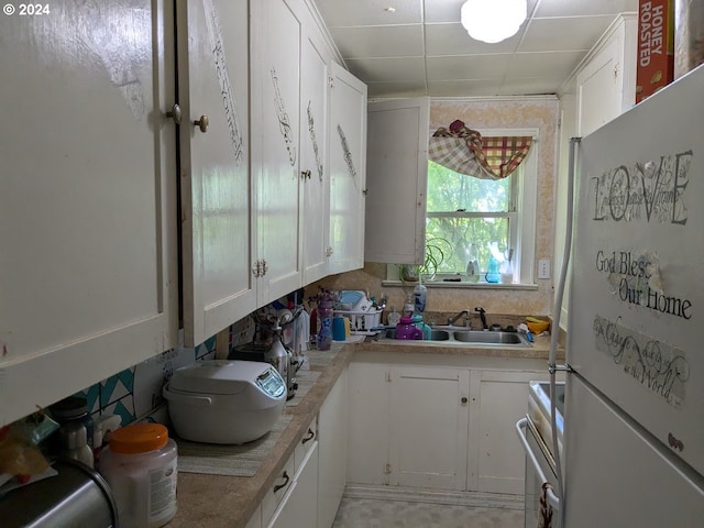 kitchen featuring white cabinetry, stainless steel stove, white refrigerator, and sink