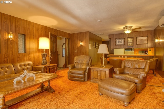 carpeted living room featuring wooden walls and ceiling fan