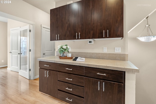 kitchen featuring tile countertops, dark brown cabinets, decorative light fixtures, and light wood-type flooring