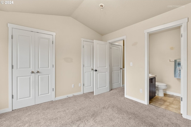 unfurnished bedroom with ensuite bathroom, light carpet, and vaulted ceiling