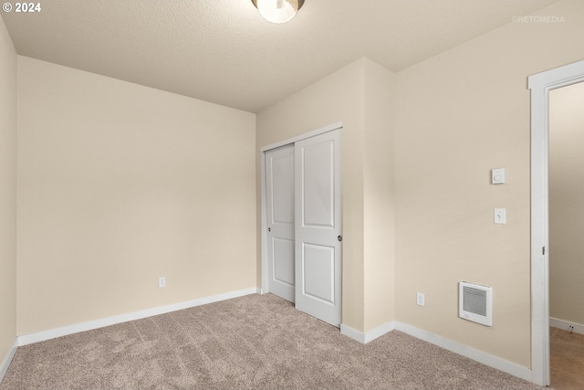 unfurnished bedroom featuring a textured ceiling, heating unit, a closet, and light colored carpet