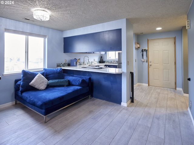 kitchen with light hardwood / wood-style flooring, stainless steel fridge, a textured ceiling, and kitchen peninsula