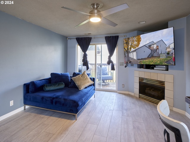 living room featuring a tiled fireplace, a textured ceiling, ceiling fan, and light wood-type flooring