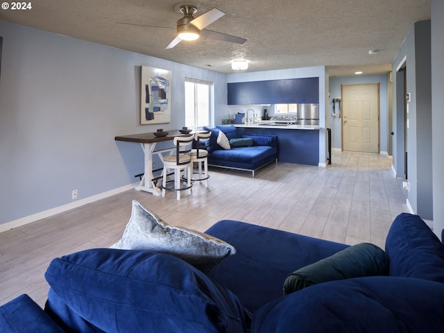 living room featuring ceiling fan, sink, a textured ceiling, and light wood-type flooring