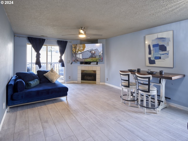 living room featuring a tiled fireplace, a textured ceiling, ceiling fan, and light hardwood / wood-style flooring