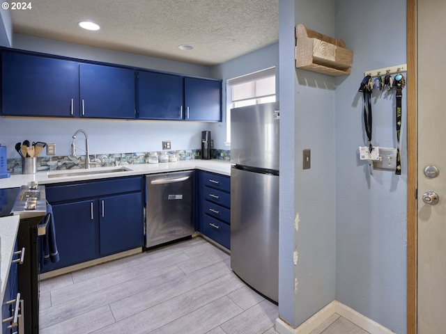 kitchen with sink, stainless steel appliances, a textured ceiling, and blue cabinetry