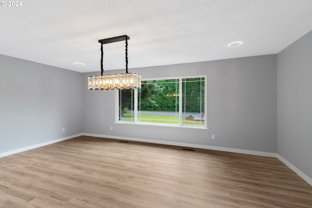 empty room with a textured ceiling, an inviting chandelier, and light hardwood / wood-style floors