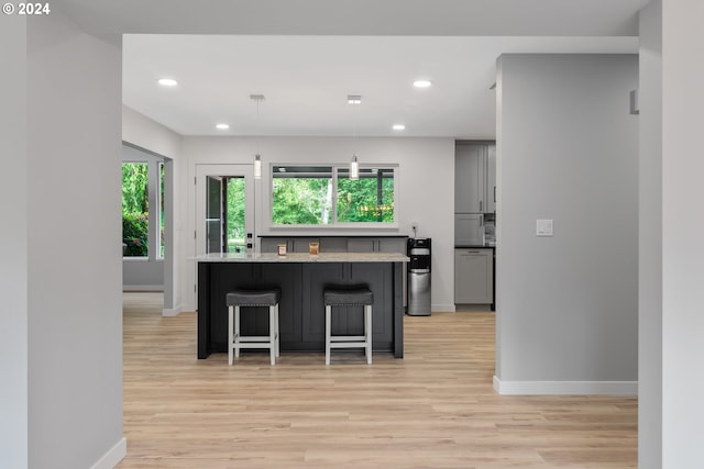 kitchen featuring light hardwood / wood-style floors, hanging light fixtures, gray cabinets, light stone counters, and a breakfast bar