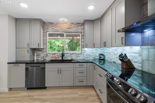 kitchen with light hardwood / wood-style floors, appliances with stainless steel finishes, gray cabinetry, wall chimney exhaust hood, and sink