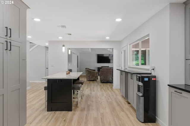 kitchen featuring light hardwood / wood-style floors, a center island, a breakfast bar, hanging light fixtures, and dark stone counters