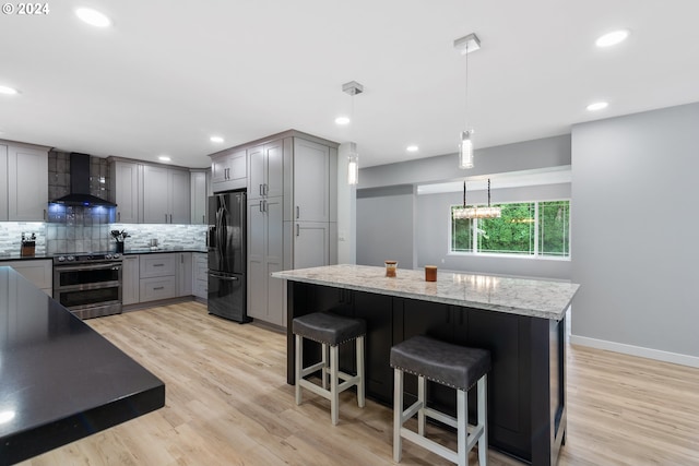 kitchen featuring pendant lighting, wall chimney exhaust hood, range with two ovens, black fridge with ice dispenser, and gray cabinetry