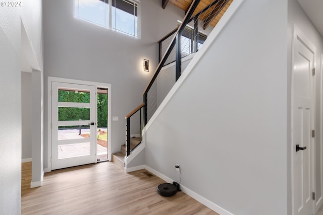 entryway featuring wood ceiling, beamed ceiling, a high ceiling, and light hardwood / wood-style flooring