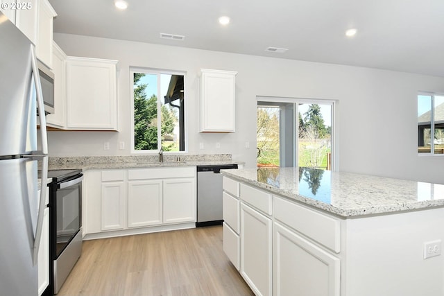 kitchen with a center island, white cabinets, light hardwood / wood-style flooring, stainless steel appliances, and light stone counters