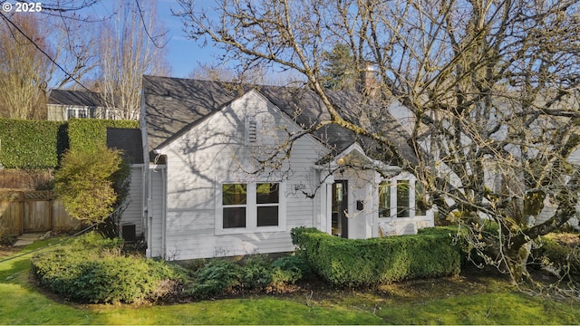 view of front facade with a front yard, roof with shingles, and fence